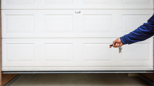 A person is holding a pair of keys in front of a garage door.