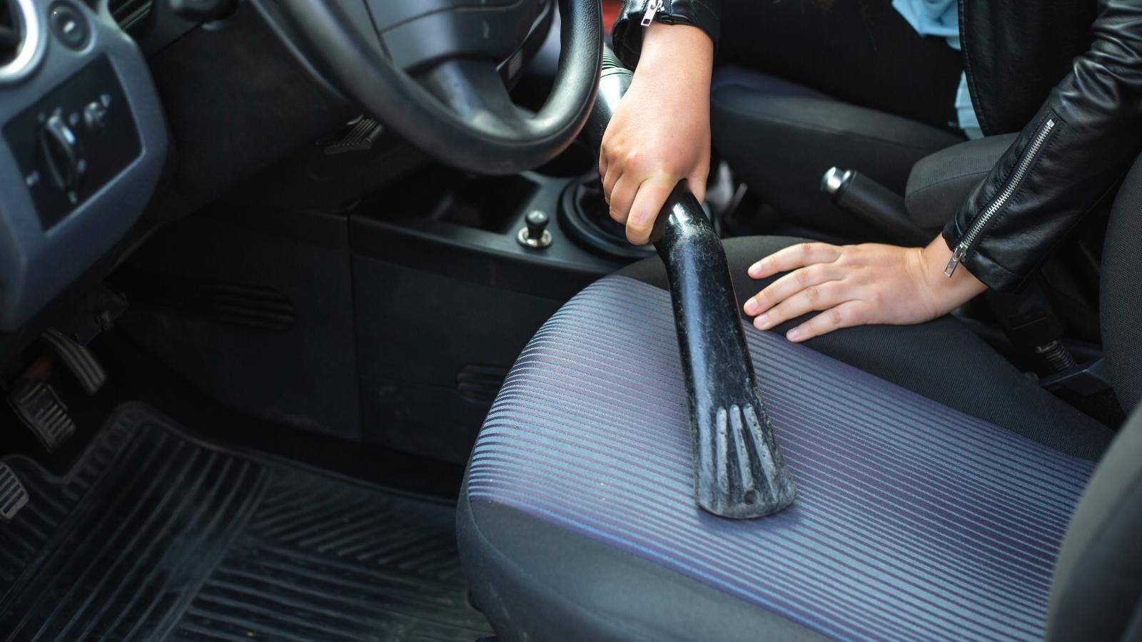 A person is cleaning a car seat with a vacuum cleaner.