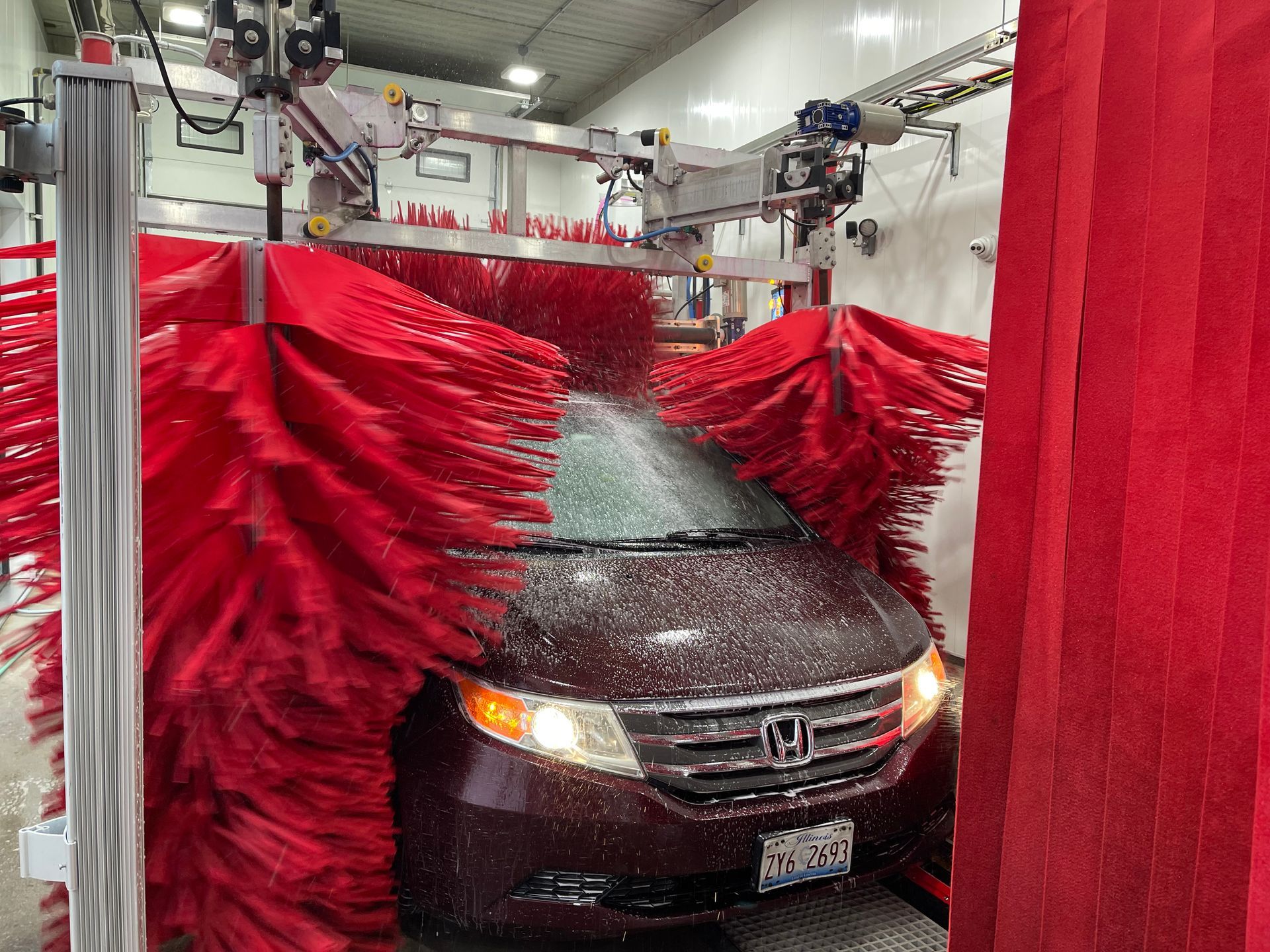 A car is going through a car wash with red brushes.
