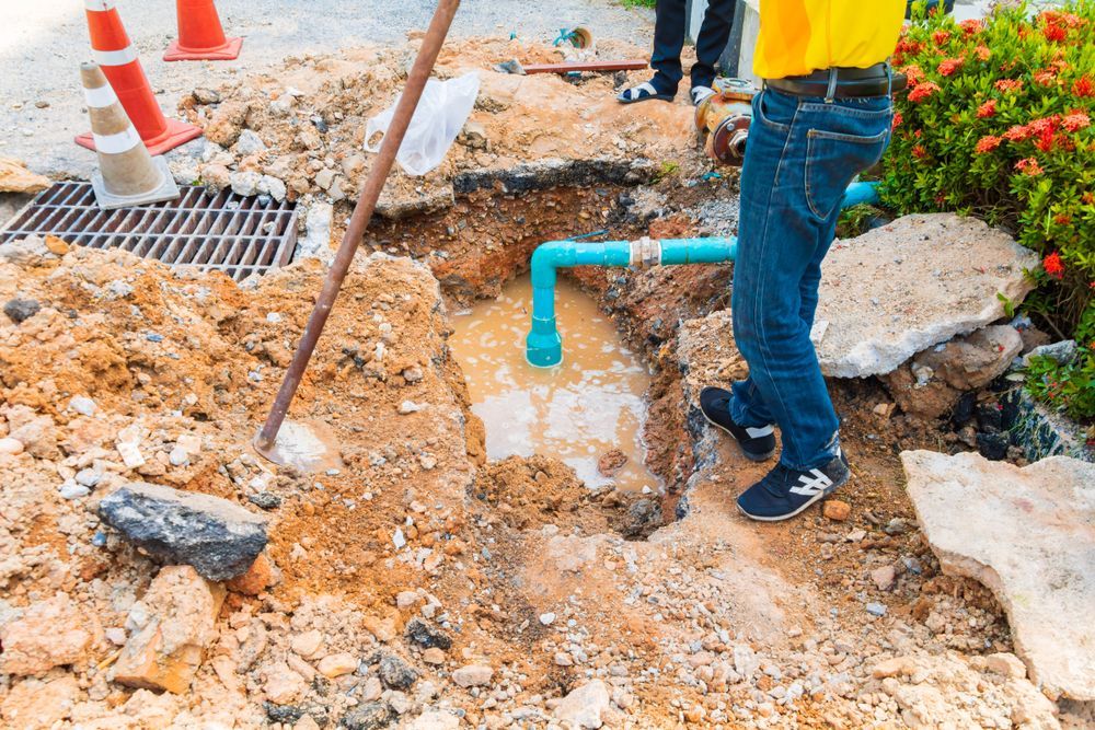 A Man Is Standing In The Dirt Next To A Pipe — Christians Plumbing in Emerald, QLD