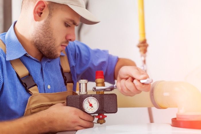 A Man Is Working On A Water Heater With A Pair Of Pliers — Christians Plumbing in Emerald, QLD