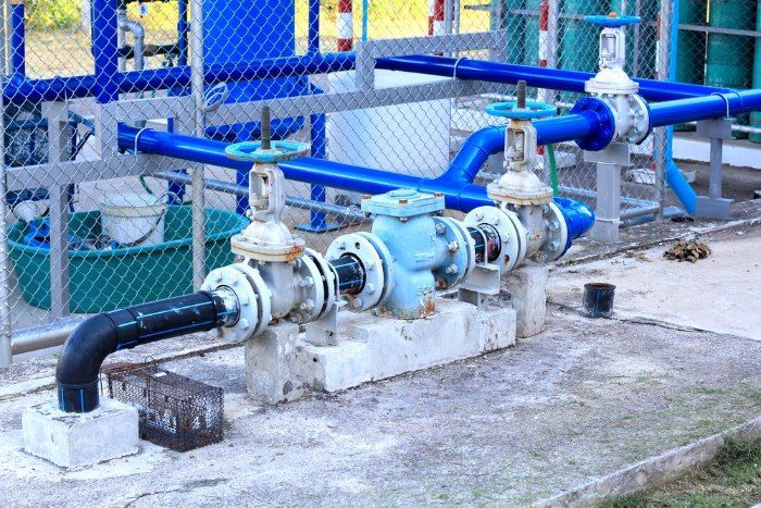 A Bunch Of Blue Pipes Are Connected To Each Other In A Fenced In Area — Christians Plumbing in Emerald, QLD