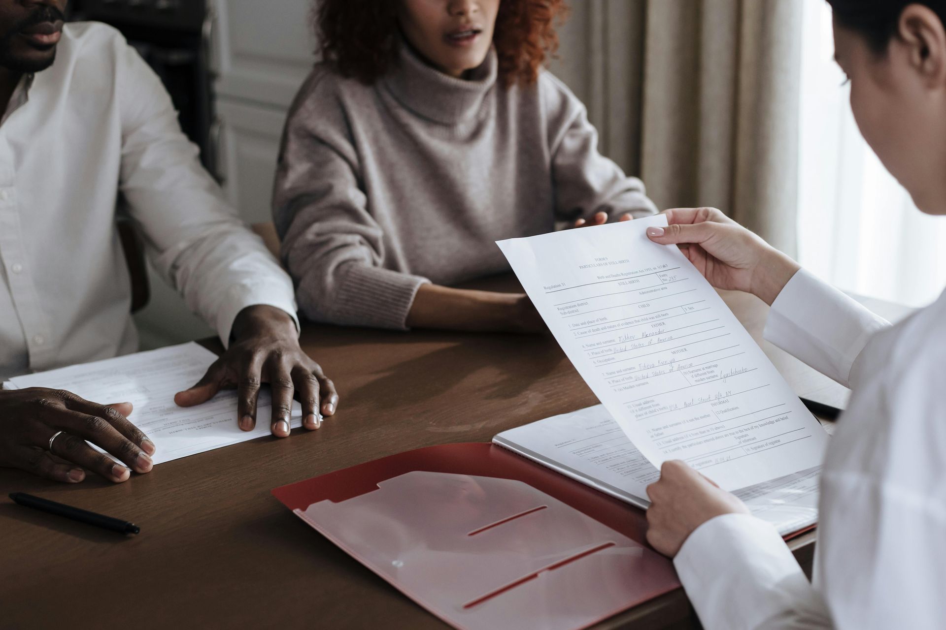 A woman is holding a piece of paper in front of a man and woman sitting at a table.