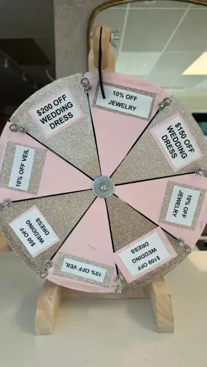Spinning prize wheel with wedding dress and jewelry discounts, pink and gold design.