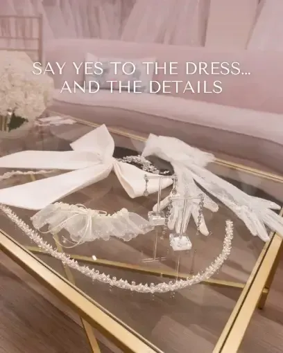 Wedding accessories displayed on a glass table: veil, gloves, headbands, and bow.