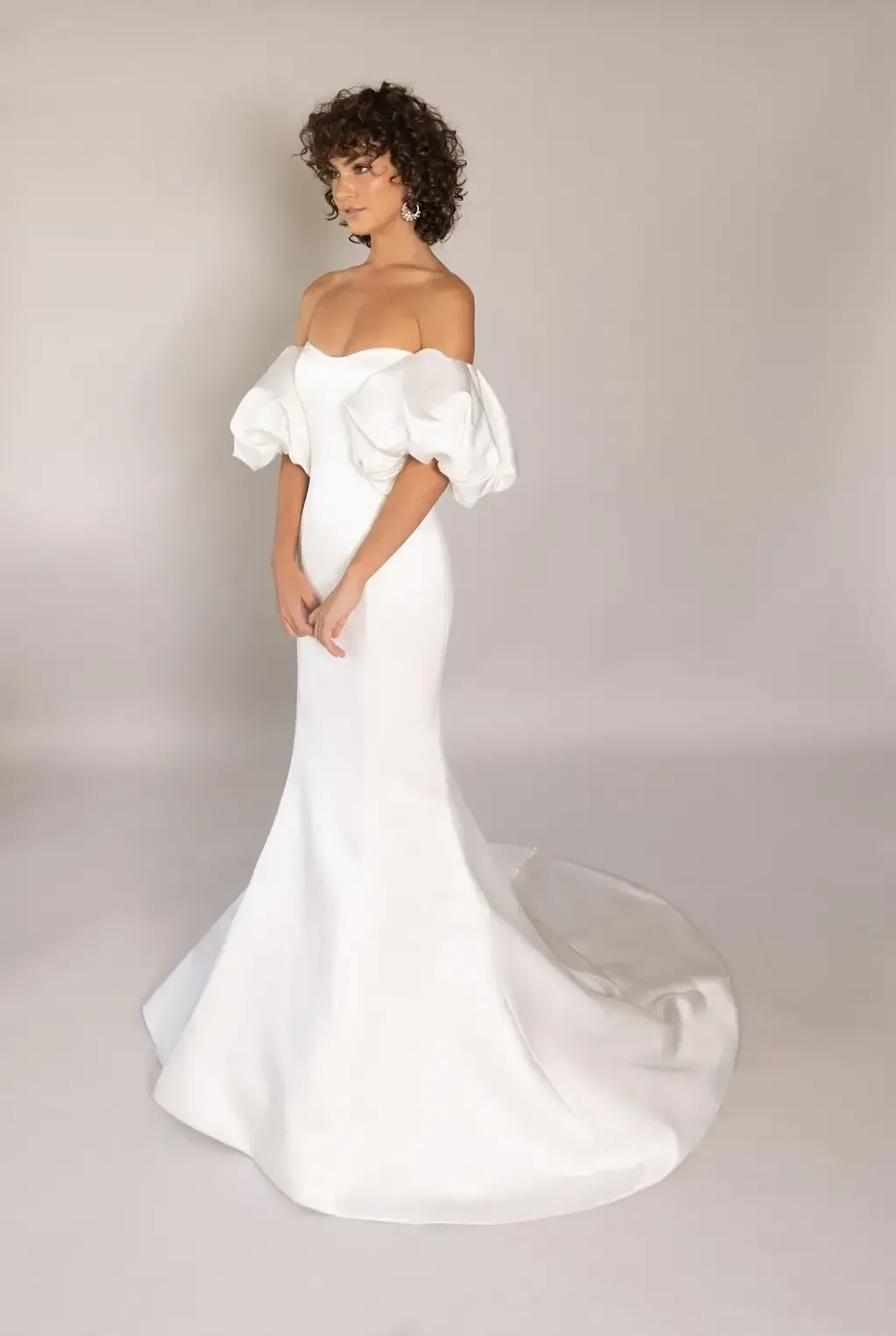 Woman in white strapless gown poses outdoors. Flowing skirt, long blonde hair, sunlit garden backdrop.