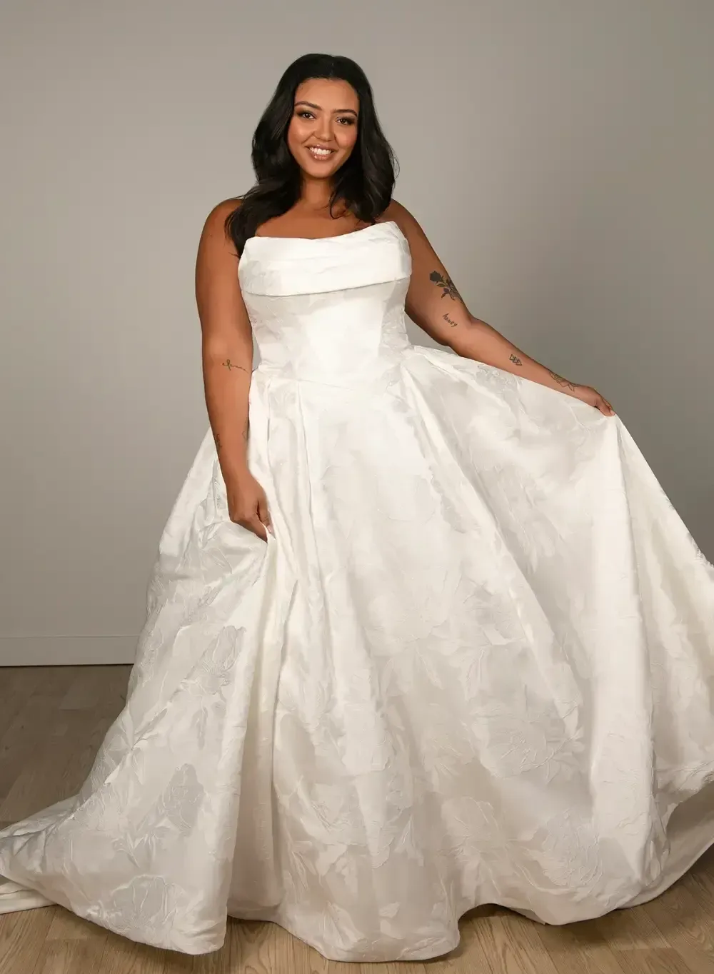 Woman wearing a white strapless wedding gown, smiling, in a studio setting.