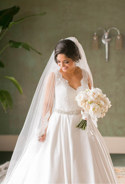 Bride in white wedding dress holding bouquet, smiling, indoors.