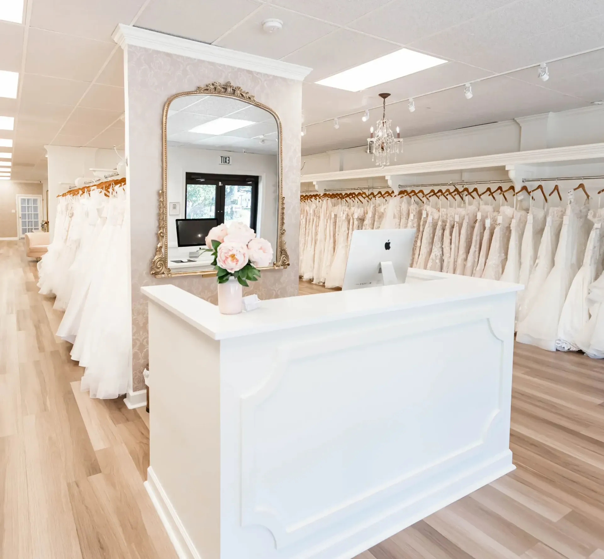 Three women smiling on a pink couch in a bridal shop, dresses in the background.