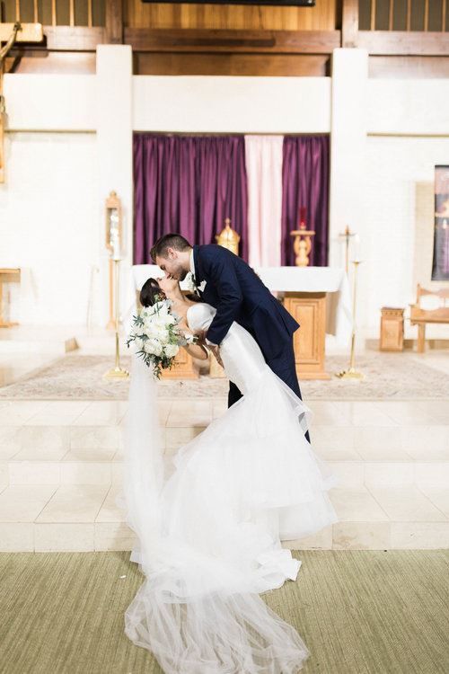 Groom dips bride for a kiss in a church during wedding ceremony.