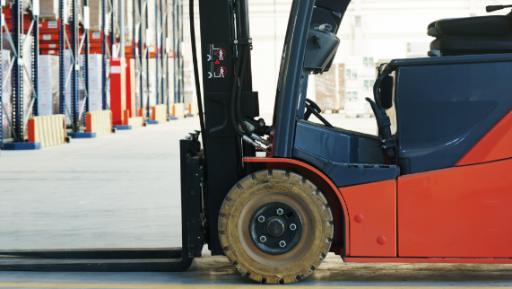 A red and blue forklift is driving down a warehouse floor.