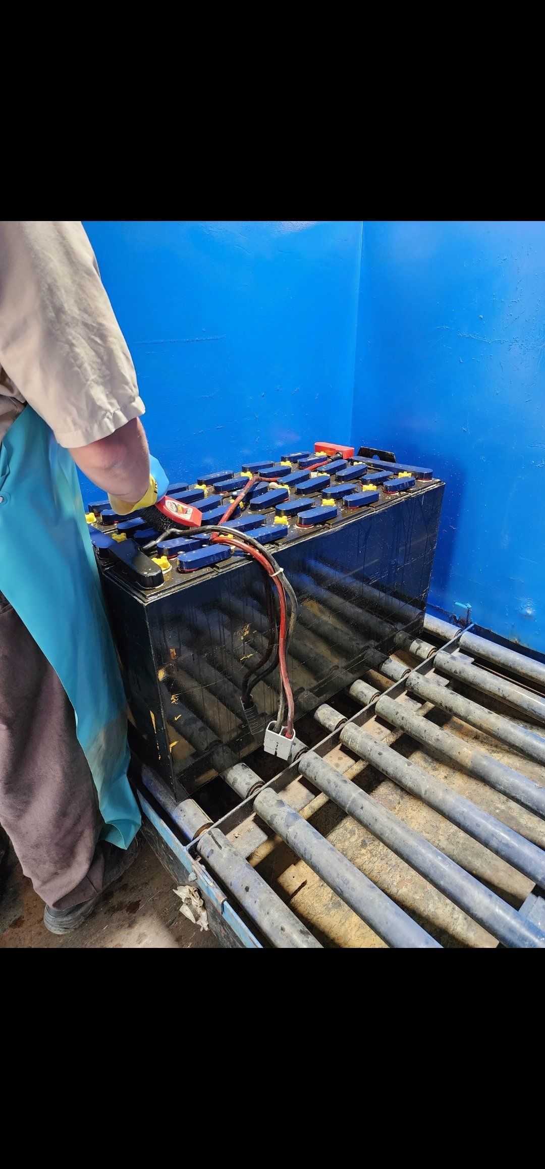 A person is working on a battery in a blue tank.