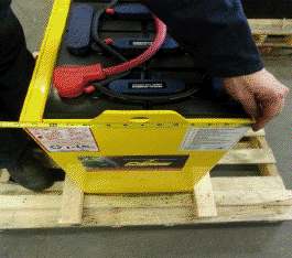 A person is holding a yellow battery on a wooden pallet.