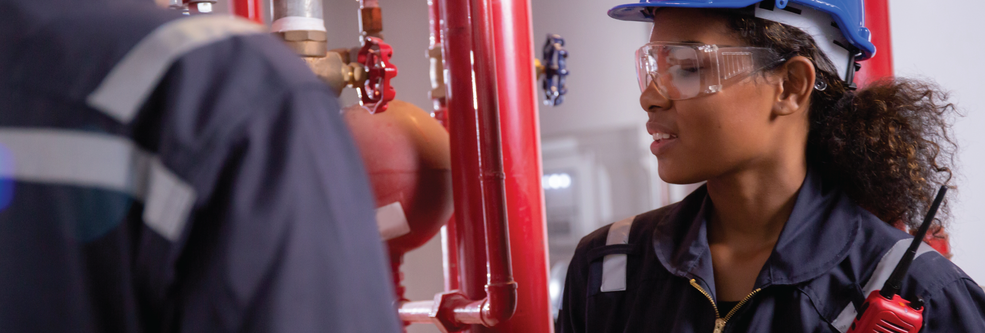 A woman in a hard hat and goggles is talking to a man in a factory.