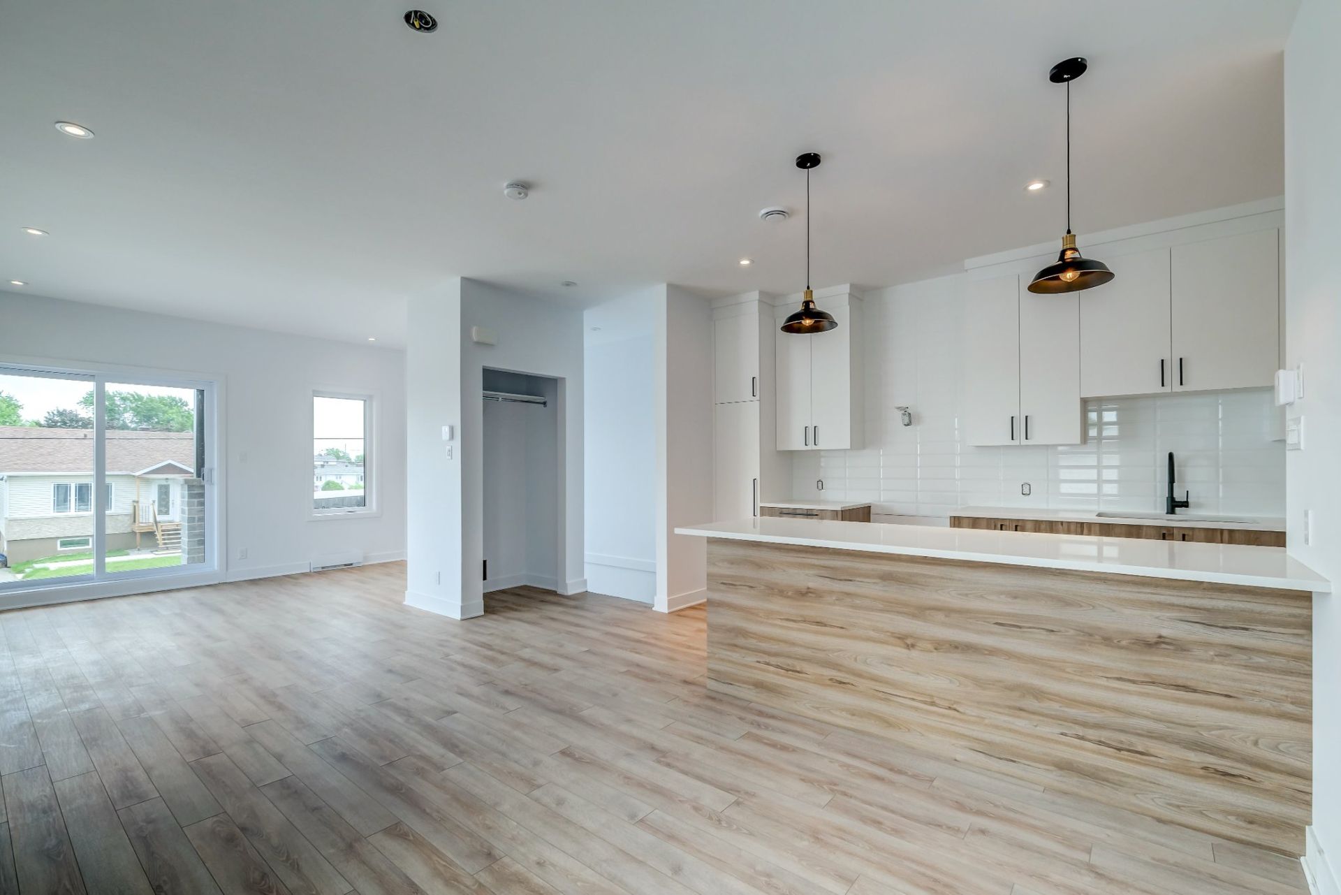 Une cuisine vide avec du parquet et des armoires blanches.