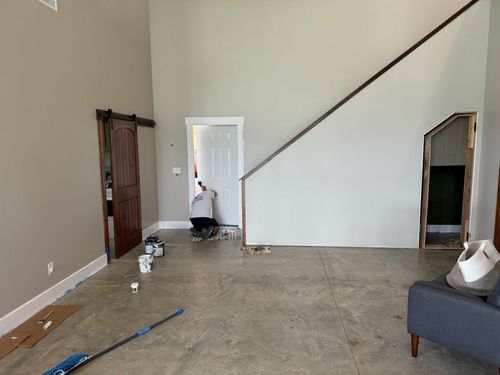 A person works on a door in a room with light grey walls, concrete floors, and two wooden door frames.