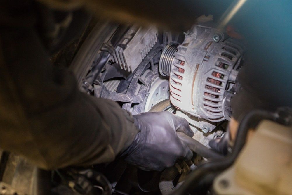 A person is working on a car engine with a flashlight.