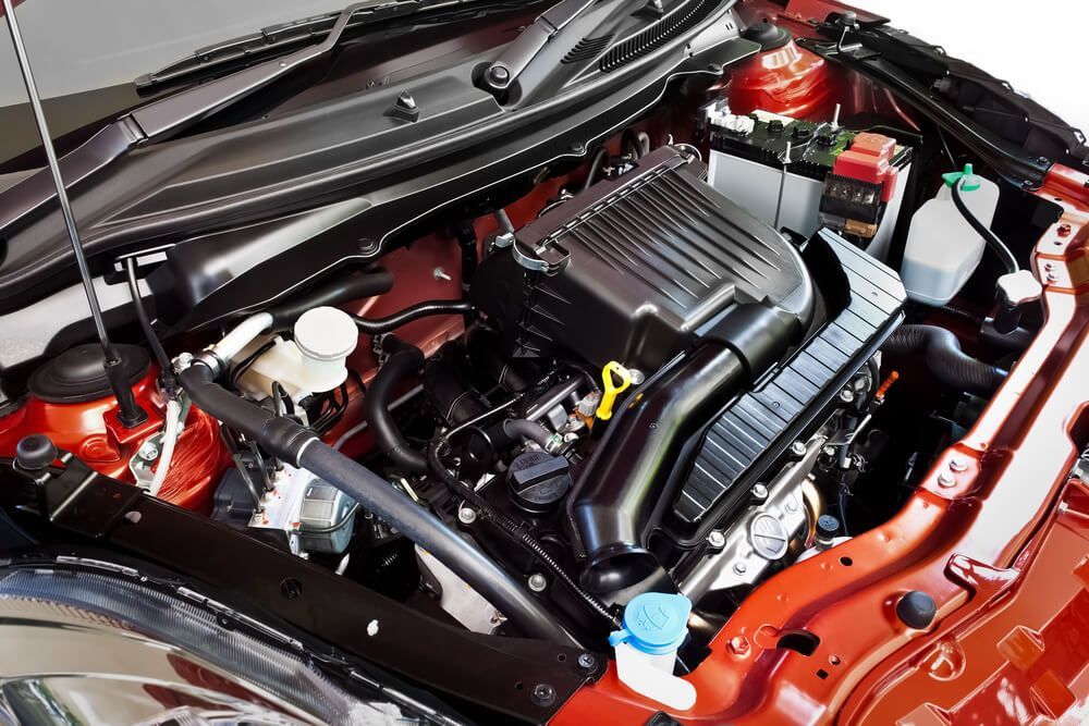 The engine of a red car is shown with the hood open.