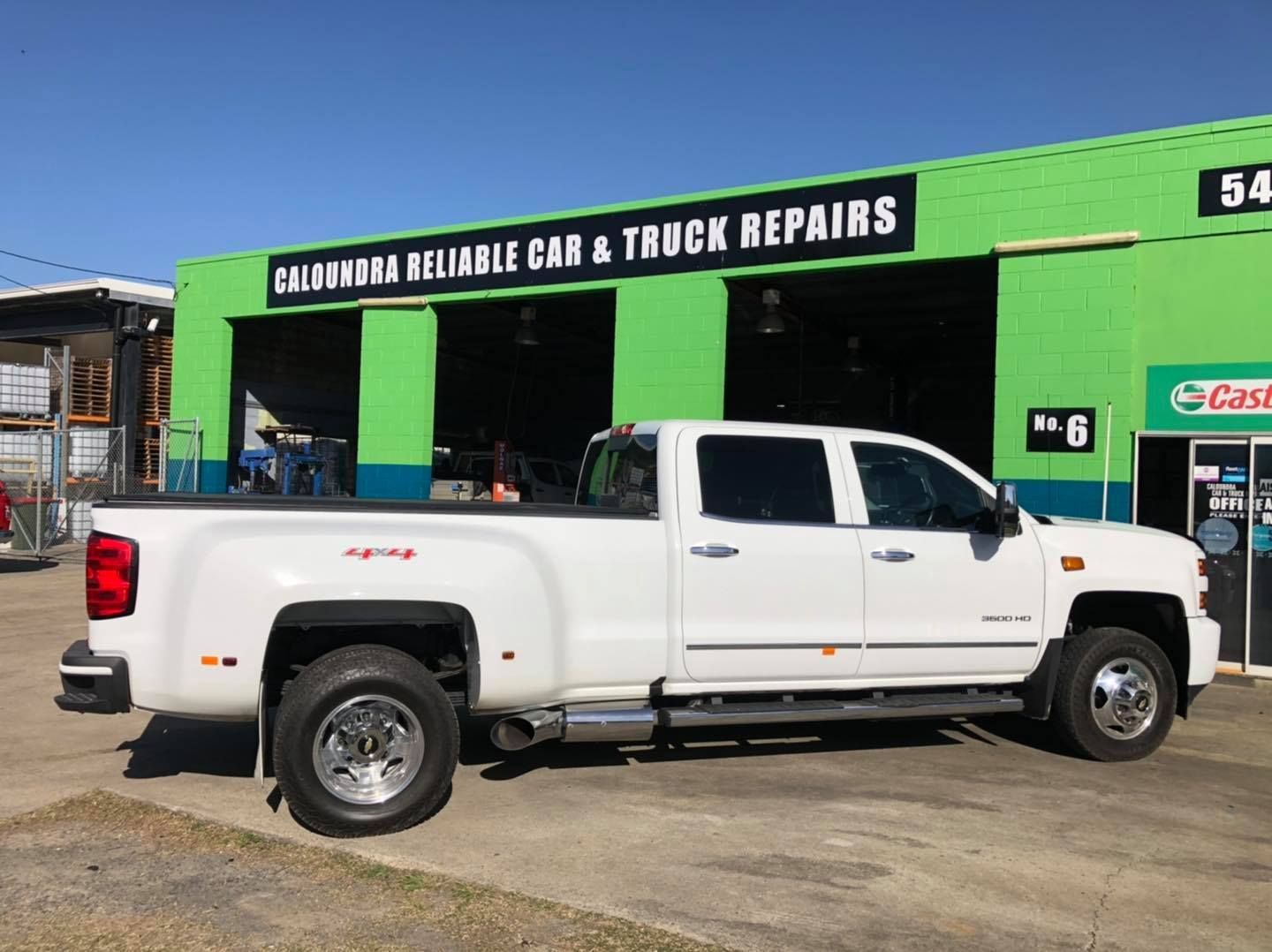 A white truck is parked in front of a car and truck repair shop.