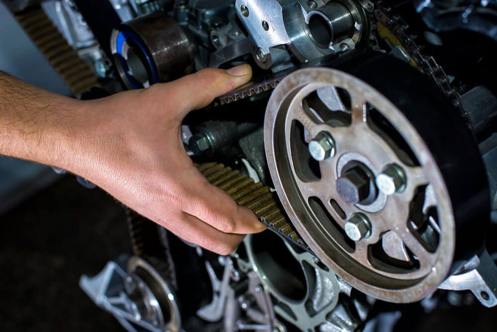A person is fixing a belt on a car engine.