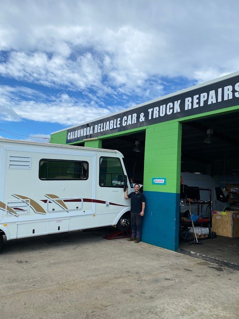 A man is standing next to a rv parked in front of a garage.