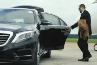 Man in suit exiting a black car on a tarmac near a plane.