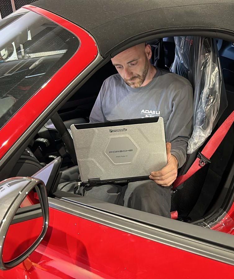 A man in a gray shirt uses a laptop inside a red car | ADAS LI
