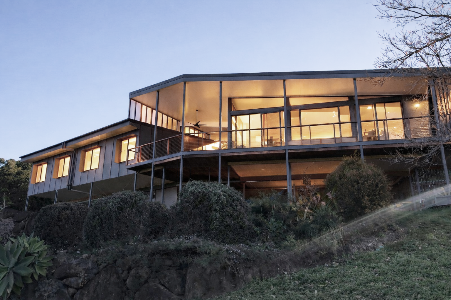 Modern house with a stone and wood facade, palm trees, and lush landscaping.