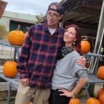 A man and a woman are posing for a picture in front of pumpkins.