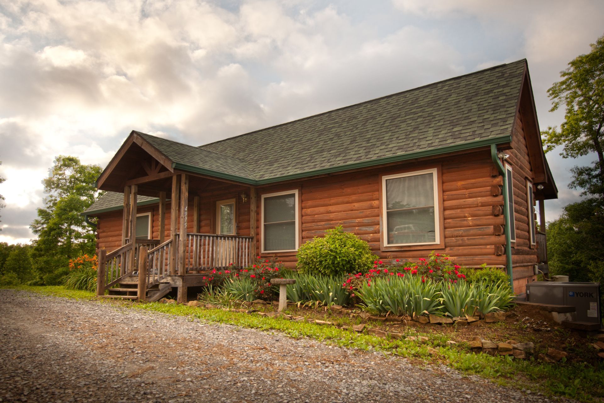 A log cabin is sitting on top of a gravel road in the middle of a forest.