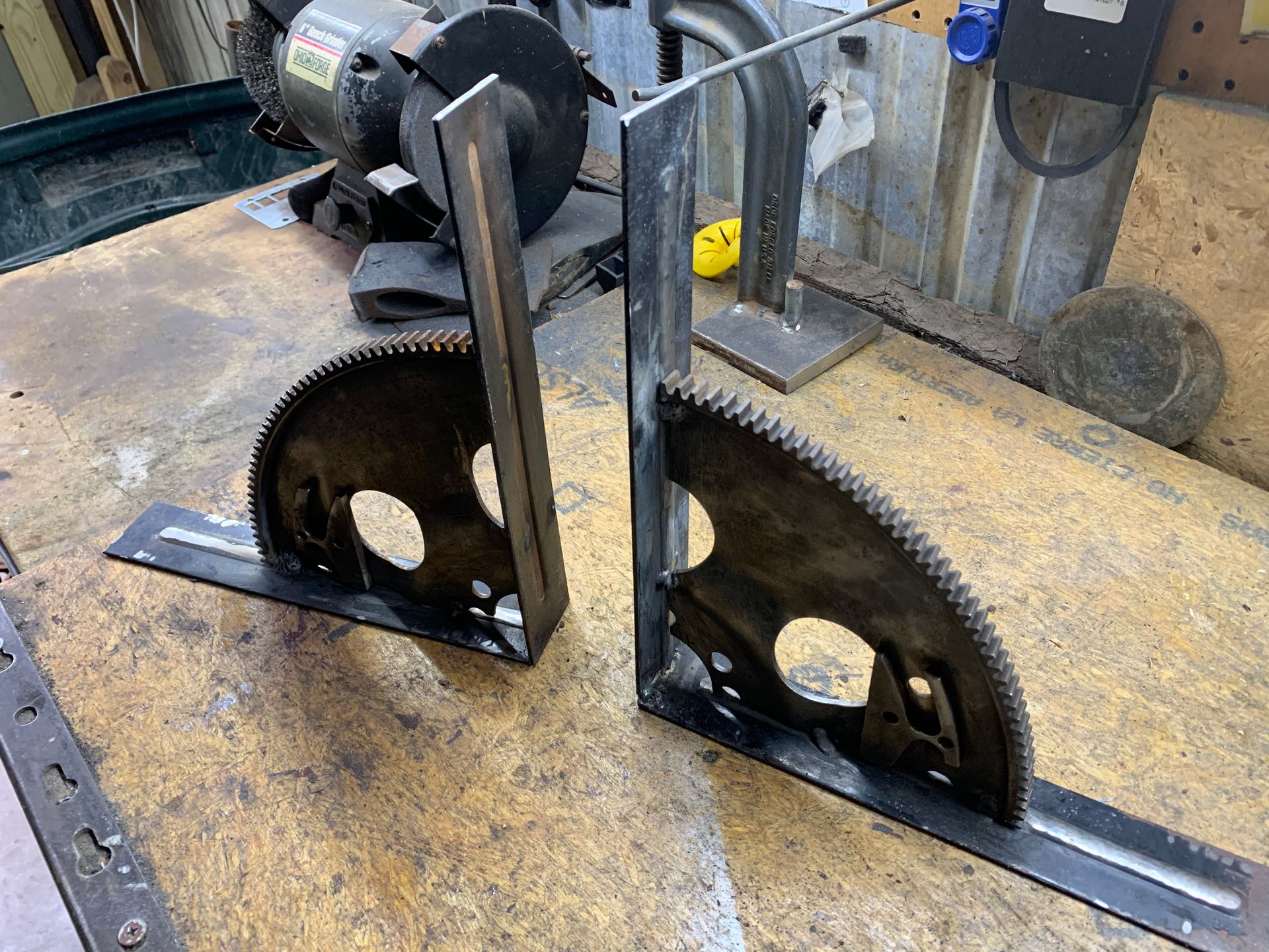 Two metal pieces are sitting on a wooden table next to a grinder.
