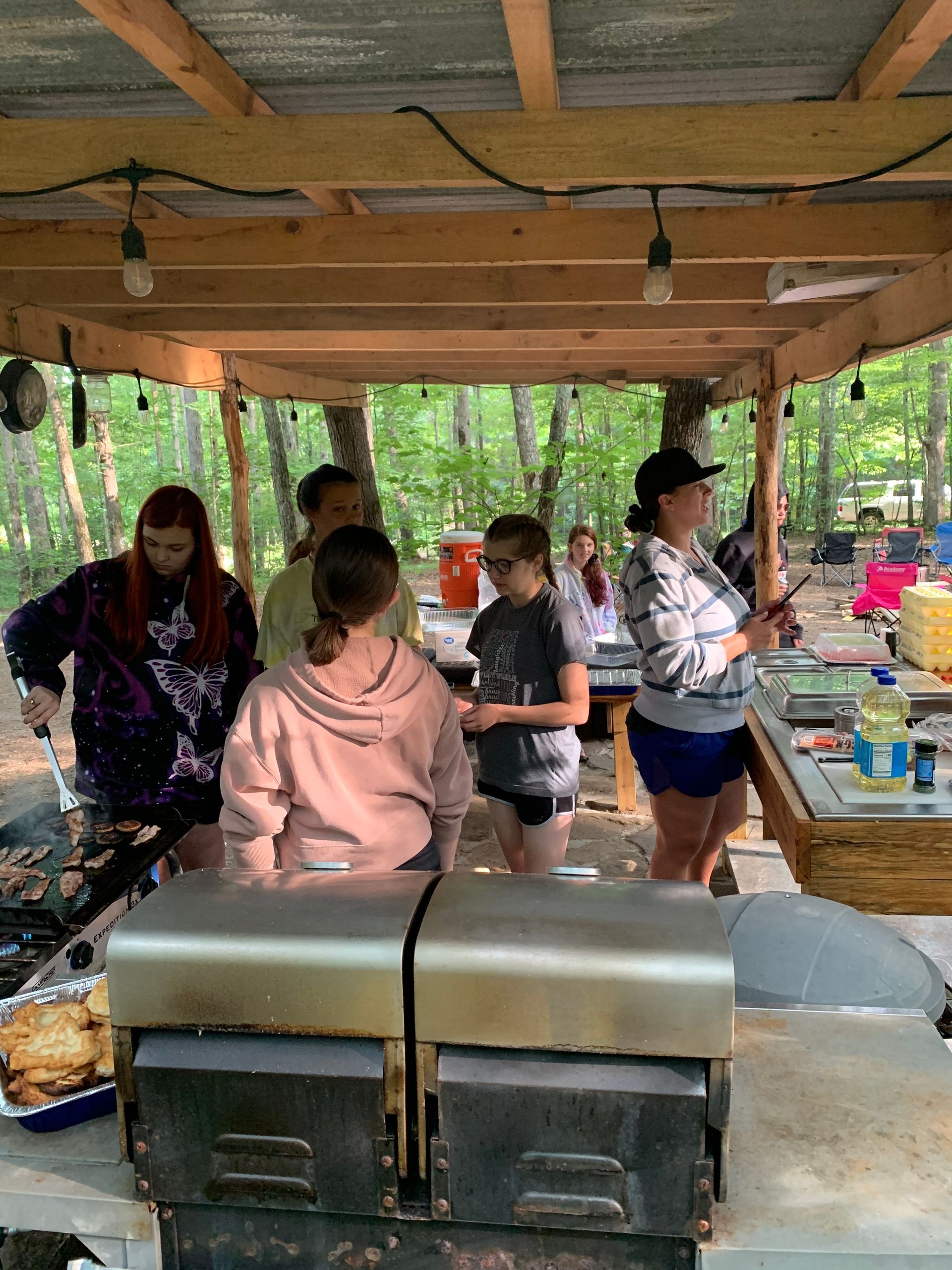 A group of people are standing around a table under a covered area.