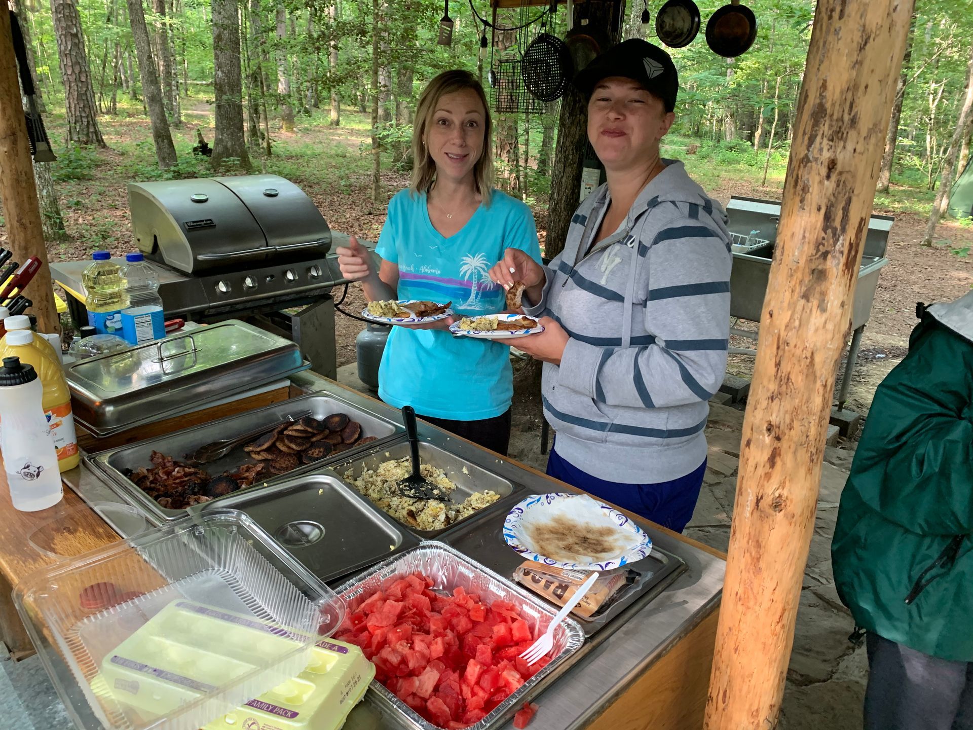 Two women are standing at a table holding plates of food.