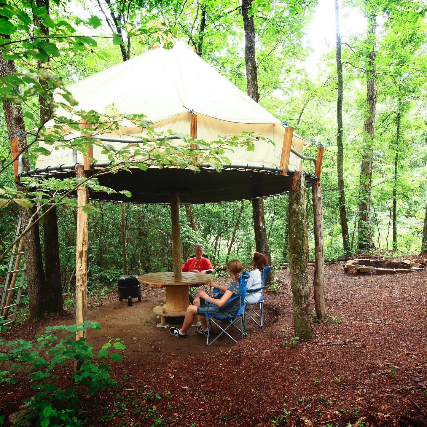 A group of people are sitting under a tent in the woods