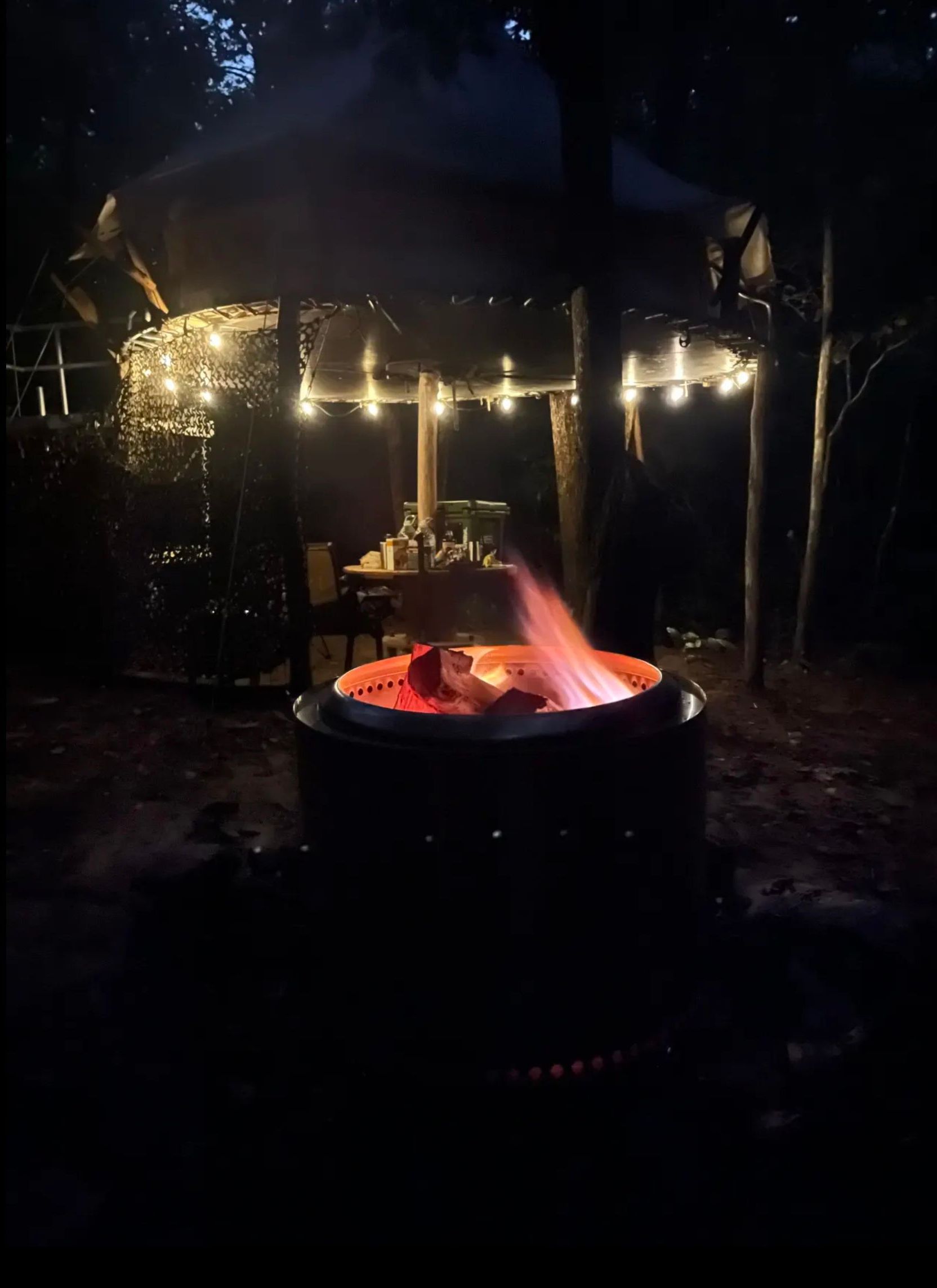A fire pit is lit up at night in front of a gazebo.