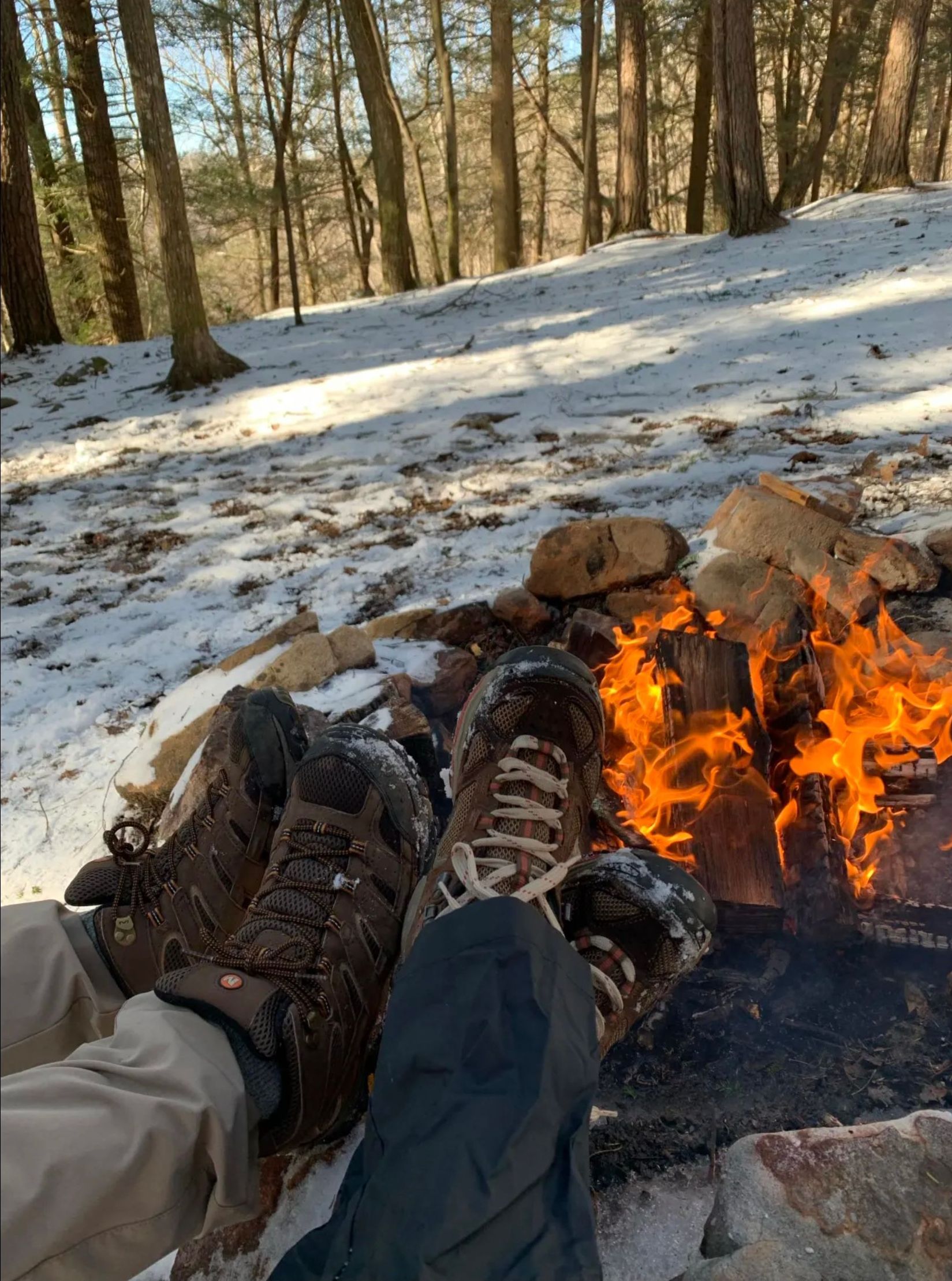 A person is laying in the snow next to a campfire.