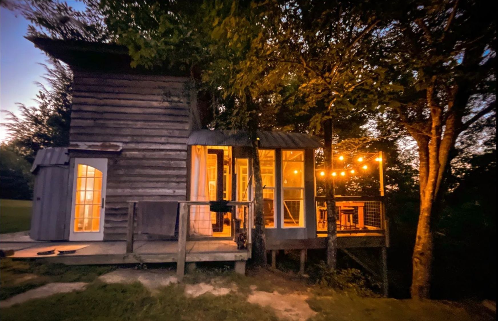 A small house with a lot of windows is lit up at night.