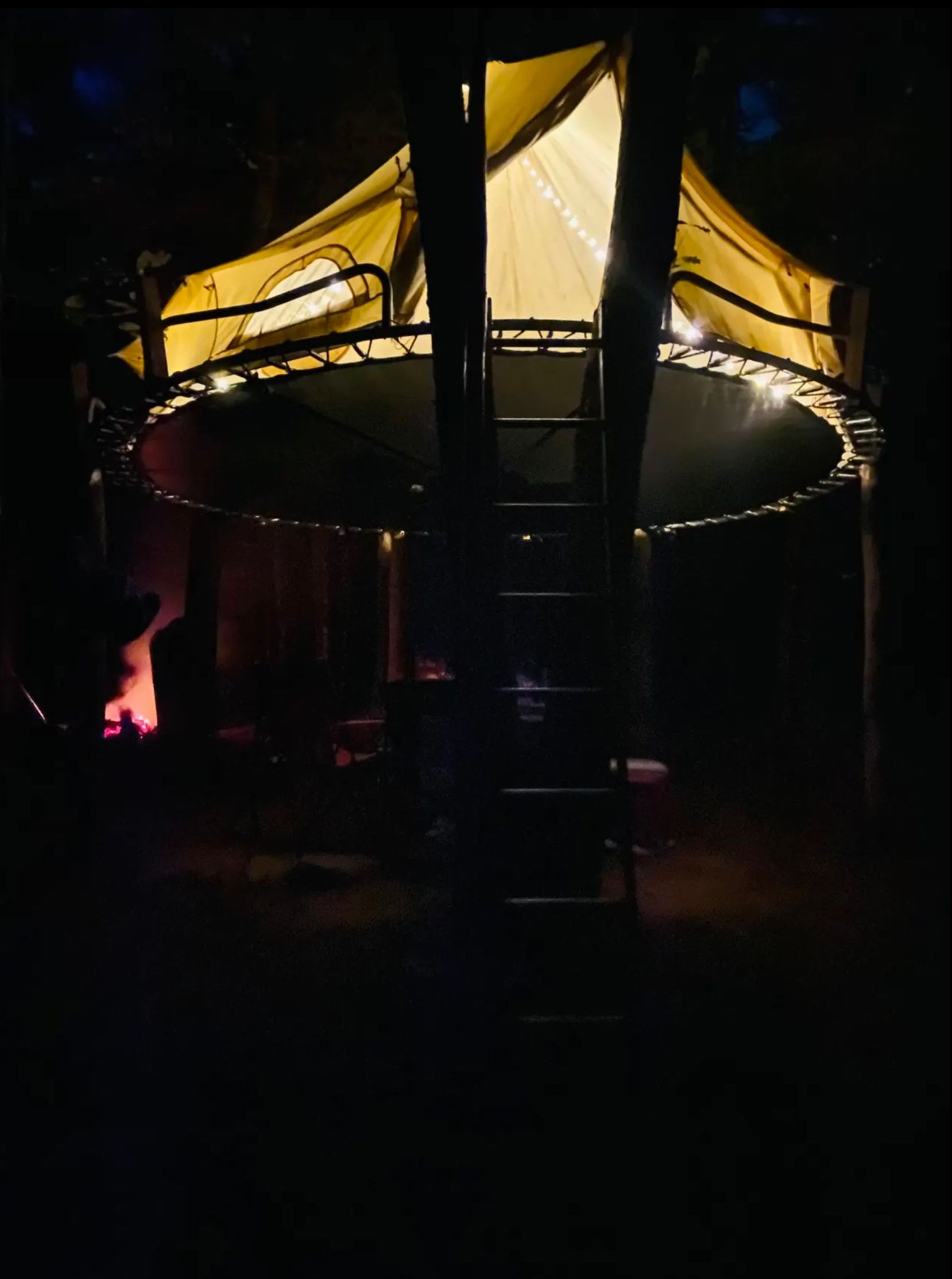 A trampoline is lit up at night with a tent in the background.