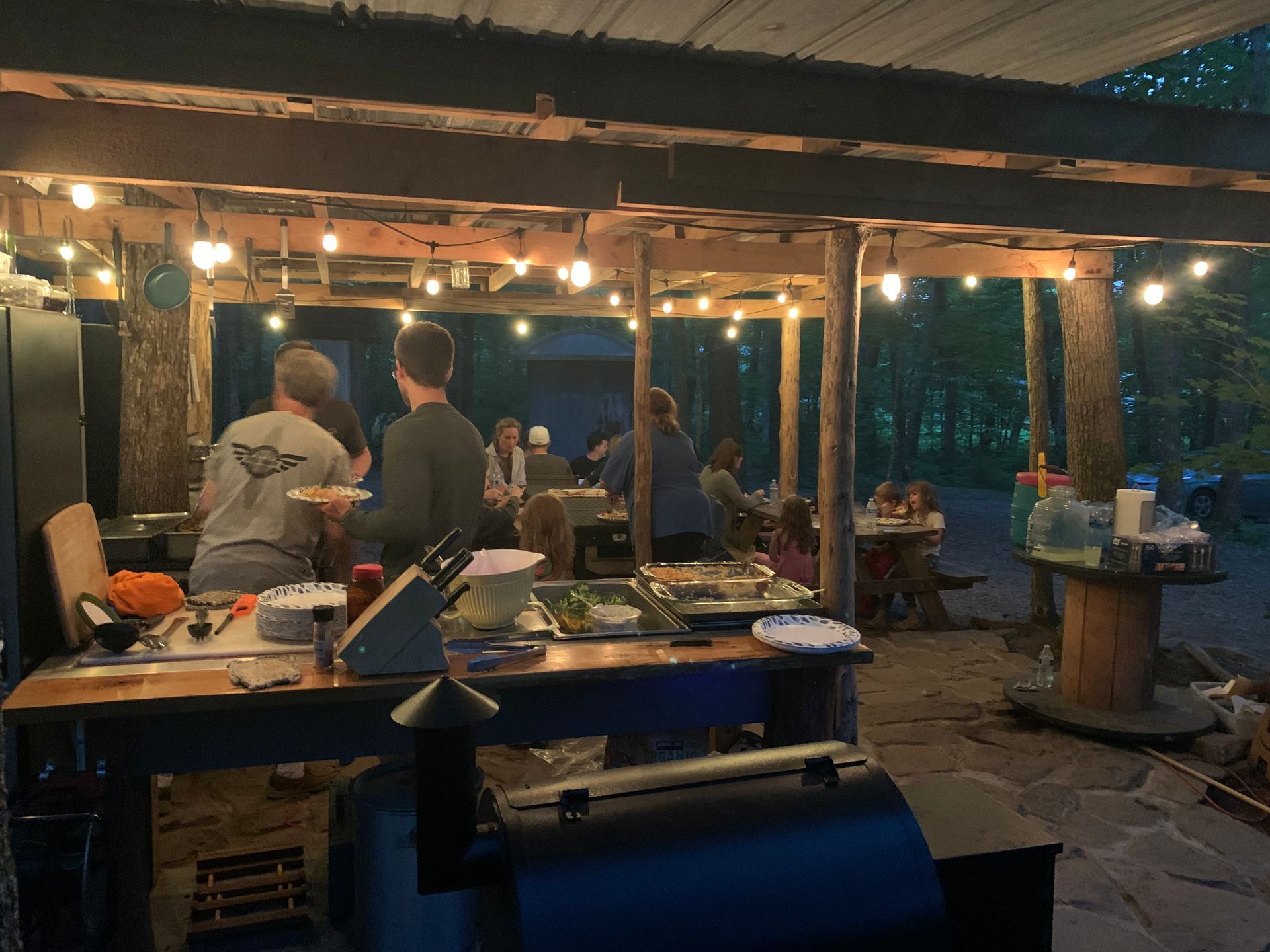 A group of people are standing around tables under a covered area.