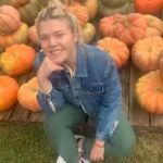 A woman is kneeling down in front of a pile of pumpkins.