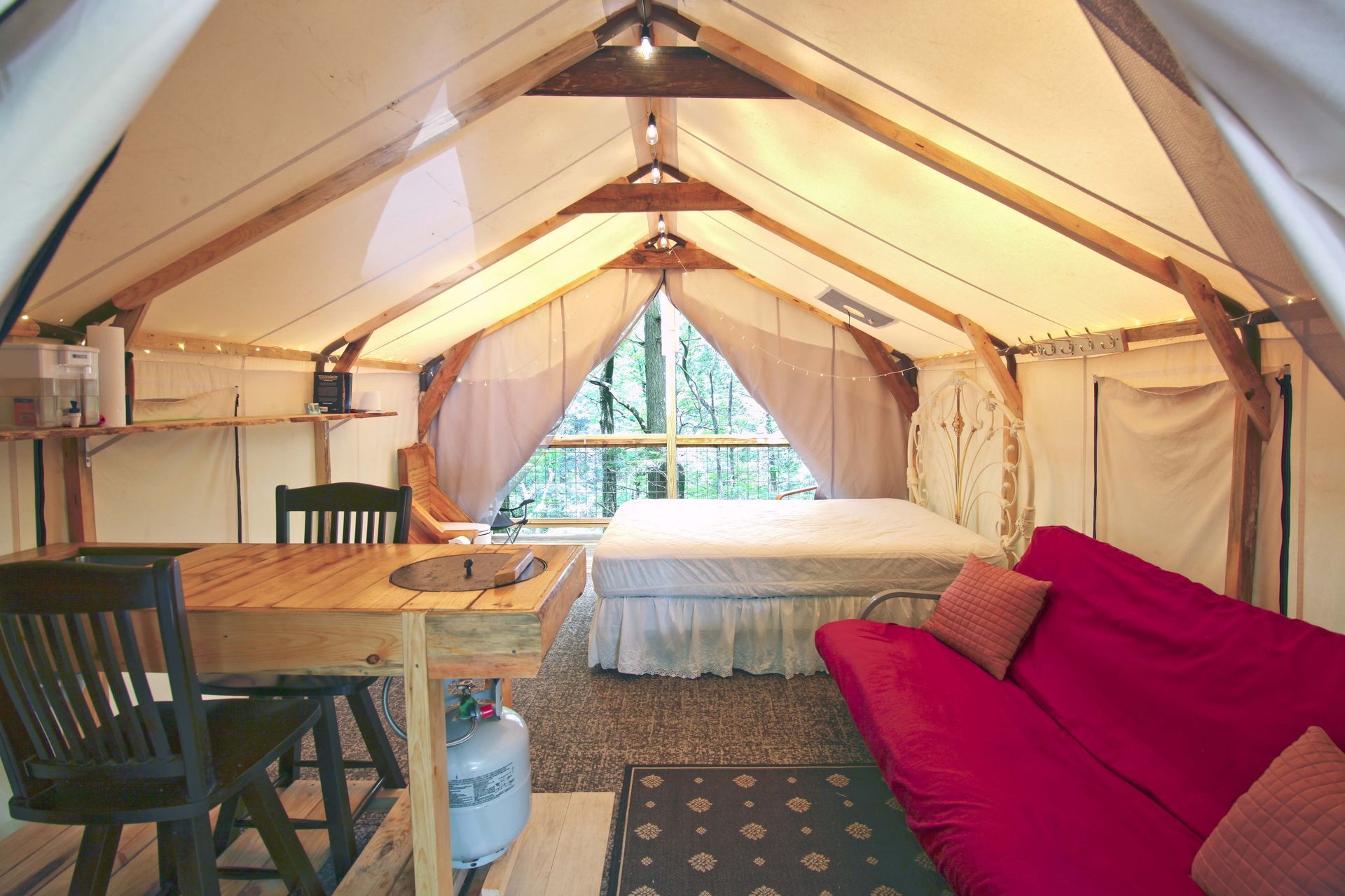 The inside of a tent with a red couch and a bed