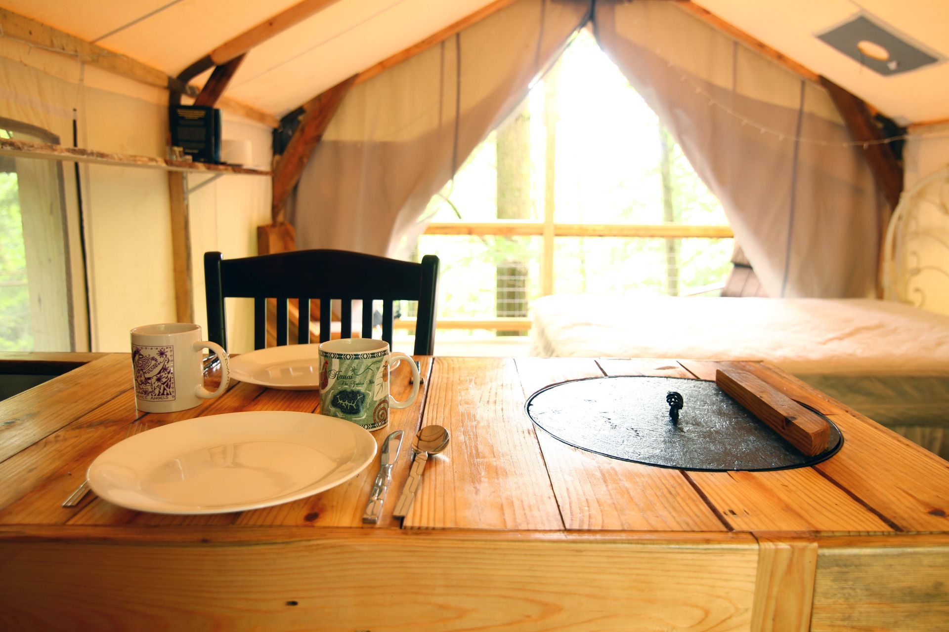 A wooden table with plates and utensils on it in a tent.