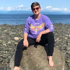 A woman is sitting on a rock on the beach.