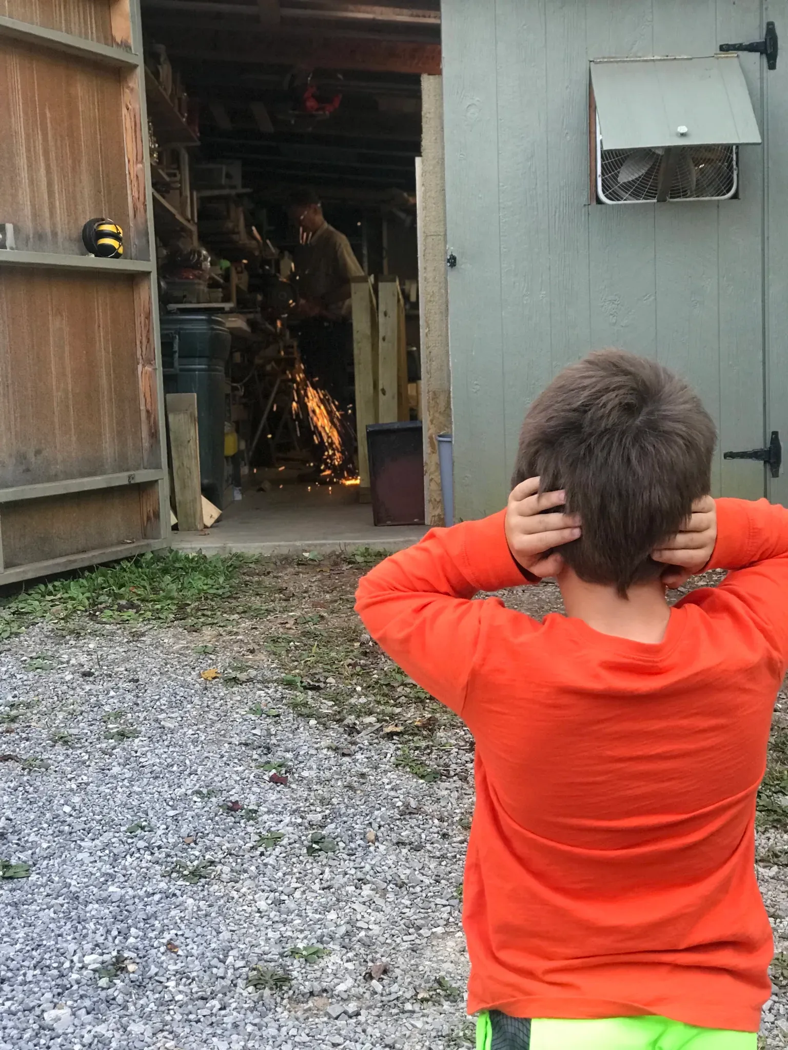 A young boy in an orange shirt is standing in front of a garage.