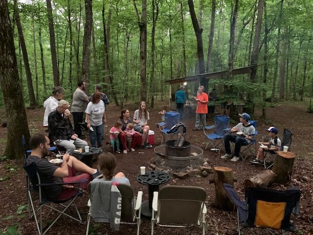 A group of people are sitting around a fire pit in the woods.