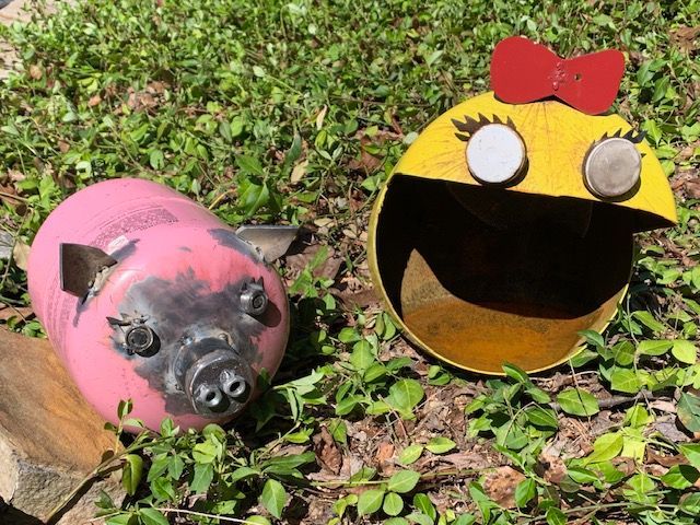 A pink pig and a yellow pac man are sitting on the grass.