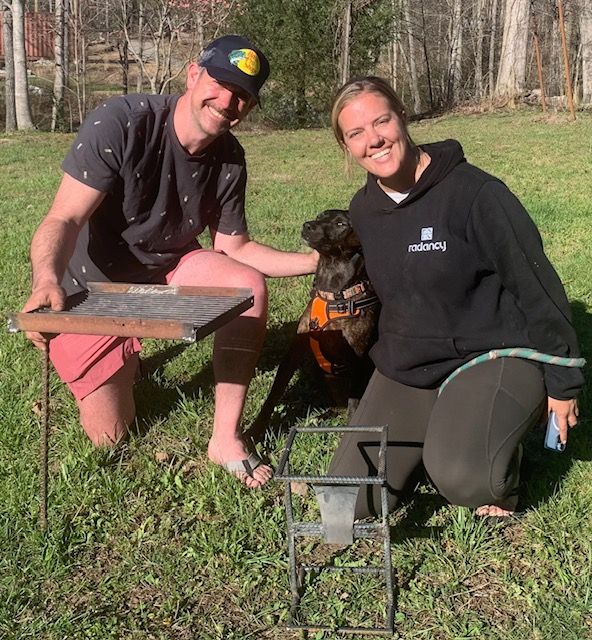 A man and a woman are kneeling in the grass with a dog