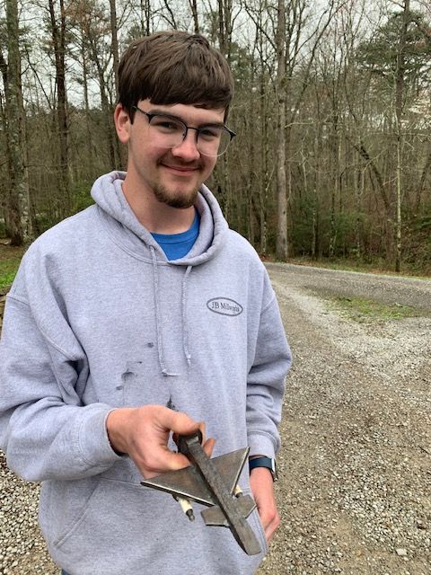 A young man wearing glasses and a grey hoodie is holding a piece of metal.