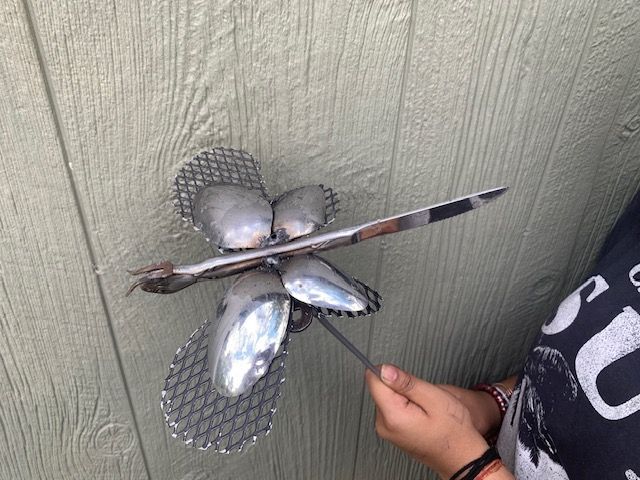 A person is holding a dragonfly made out of spoons.
