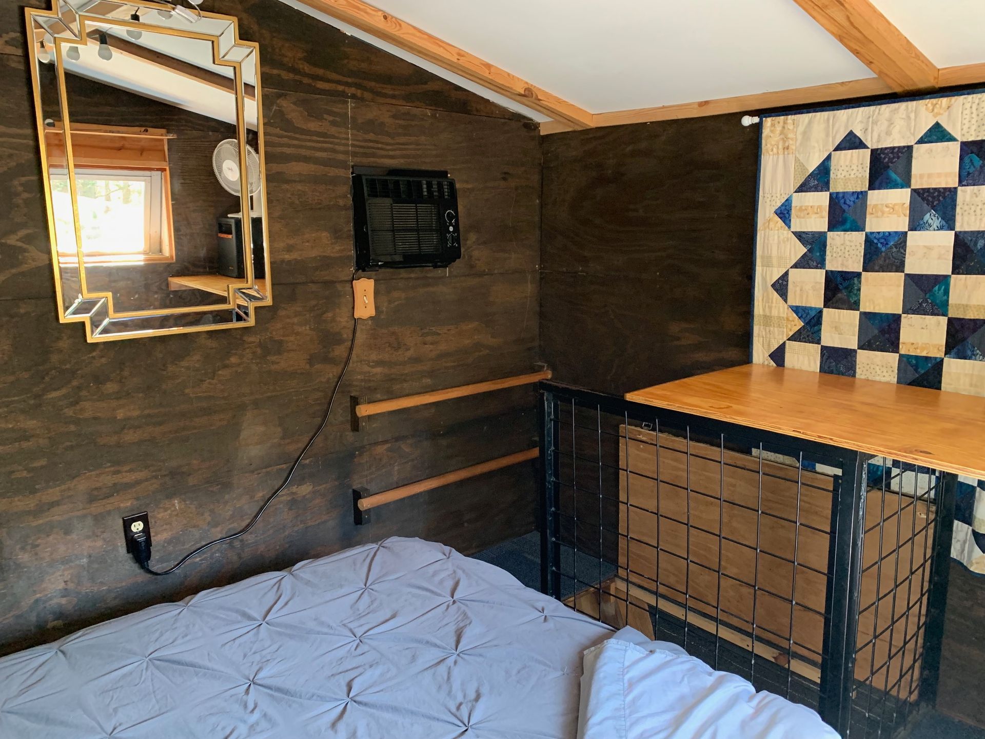 A bedroom with a bed , a mirror and a quilt on the wall.